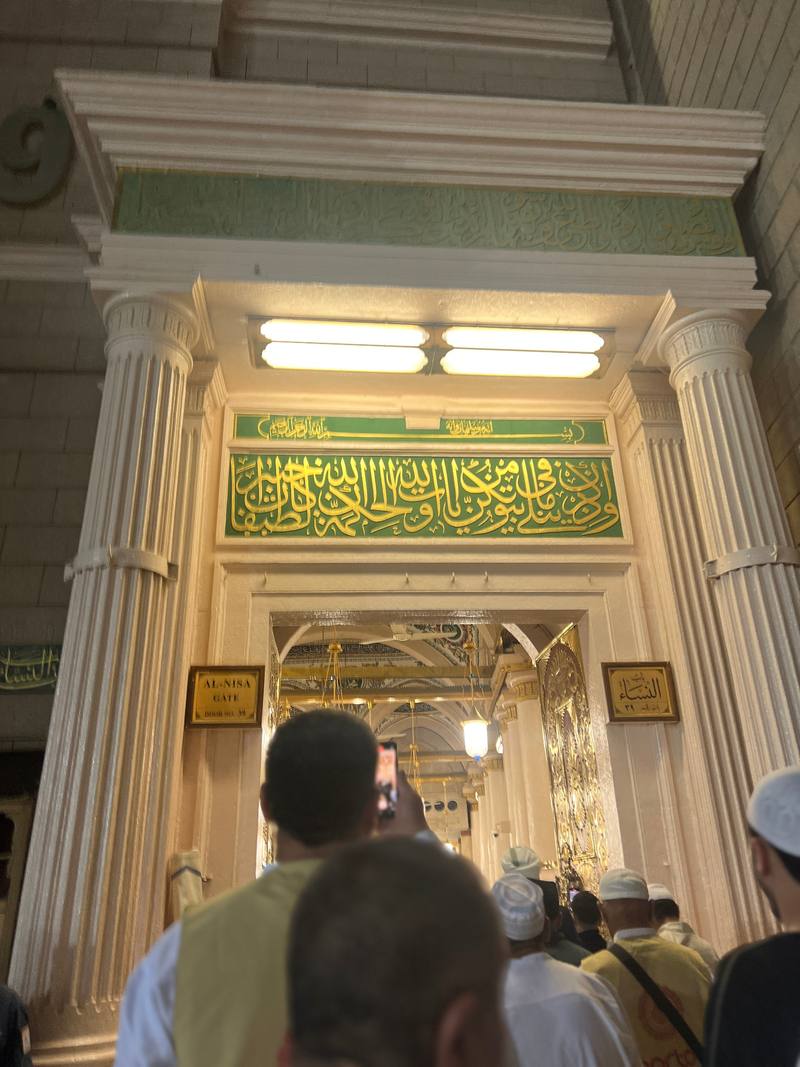 Ornate gateway in Madinah with green-and-gold Arabic calligraphy, cream stonework and warm interior light